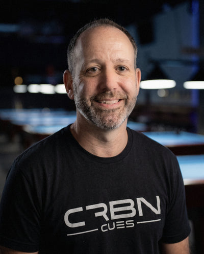 Justice Eagan, founder of CRBN Cues, smiling in a black CRBN Cues t-shirt in a pool hall