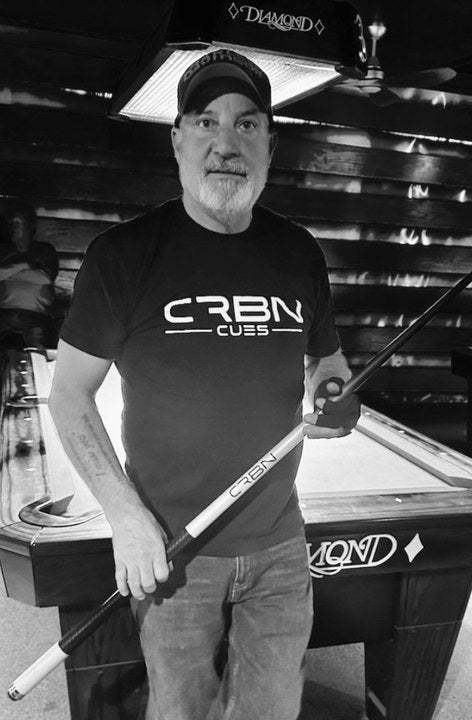 CRBN Cues customer in a CRBN Cues shirt holding his cue beside a pool table