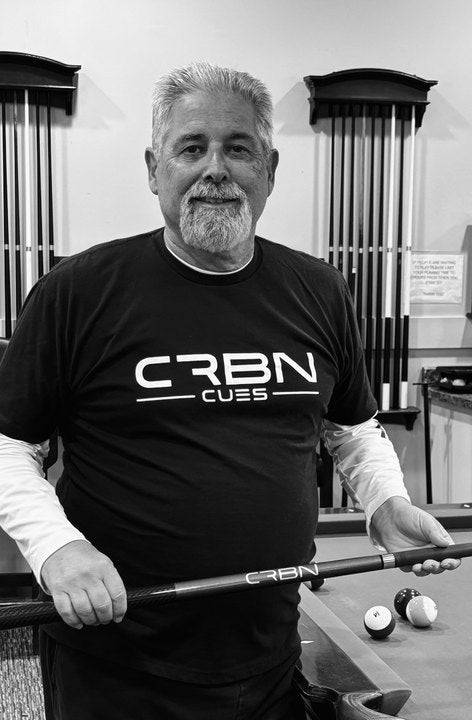 CRBN Cues customer in a CRBN Cues shirt holding his CRBN cue beside a pool table